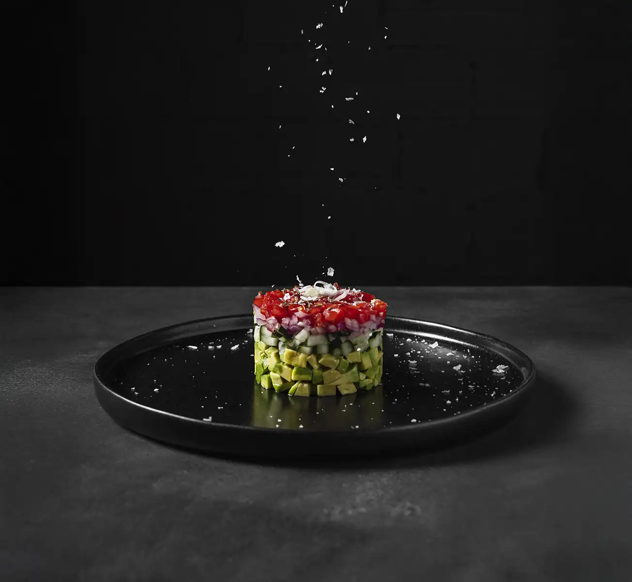 Tártaro vegetariano elegante com camadas de abacate, pepino, cebola e tomate, finalizado com flor de sal – gastronomia criativa e saudável.